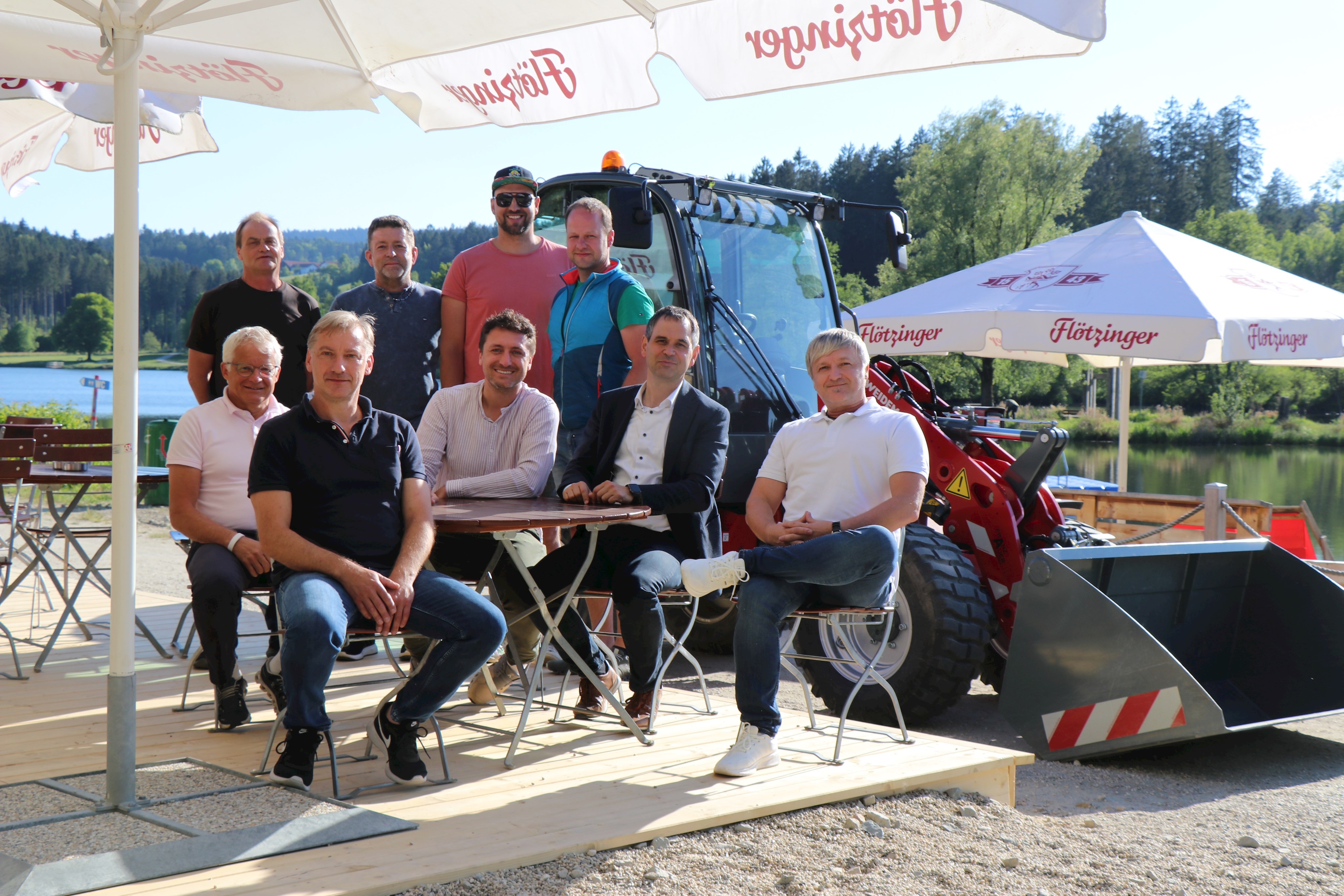 Der Rannasee ist bereit für die Badesaison 2025, davon haben sich Wegscheids Bürgermeister Christian Escherich (sitzend v.l.), Karl-Heinz Lifka (Gebäudemanagement Landkreis Passau), Andreas Meisinger (Geschäftsführer Rannasee Gastro GmbH), Landrat Raimund Kneidinger, Werner Kinateder (Gebäudemanagement Landkreis Passau), Betriebsleiter Alexander Miedl (hinten v.l.), Josef Kern (Landkreisbauhof Wegscheid), Lukas Kramler (Rannasee Gastro GmbH) und Andreas Lang (Landkreisbauhof Wegscheid) auf der neuen Holzterrasse überzeugt.