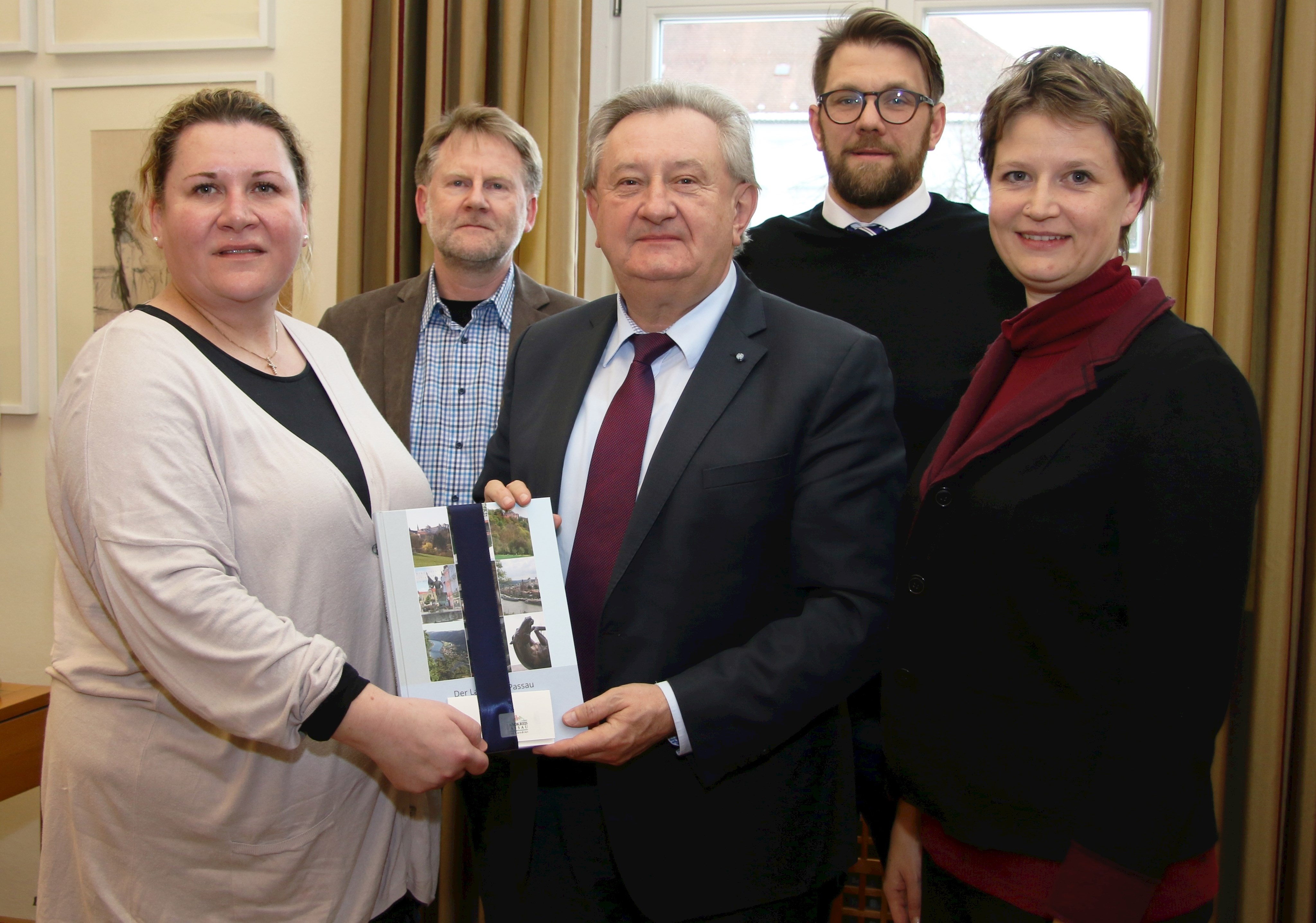 Landrat Franz Meyer überreicht Christine Halbig (links)  das Landkreisbuch und freut sich mit (v.l.) Sachgebietsleiter Soziales & Senioren Siegfried Weishäupl, Abteilungsleiter Andreas Büttner und der Geschäftsstellenleiterin der Gesundheitsregion plus Passauer Land Franziska Solger- Heinz über die Zusammenarbeit.